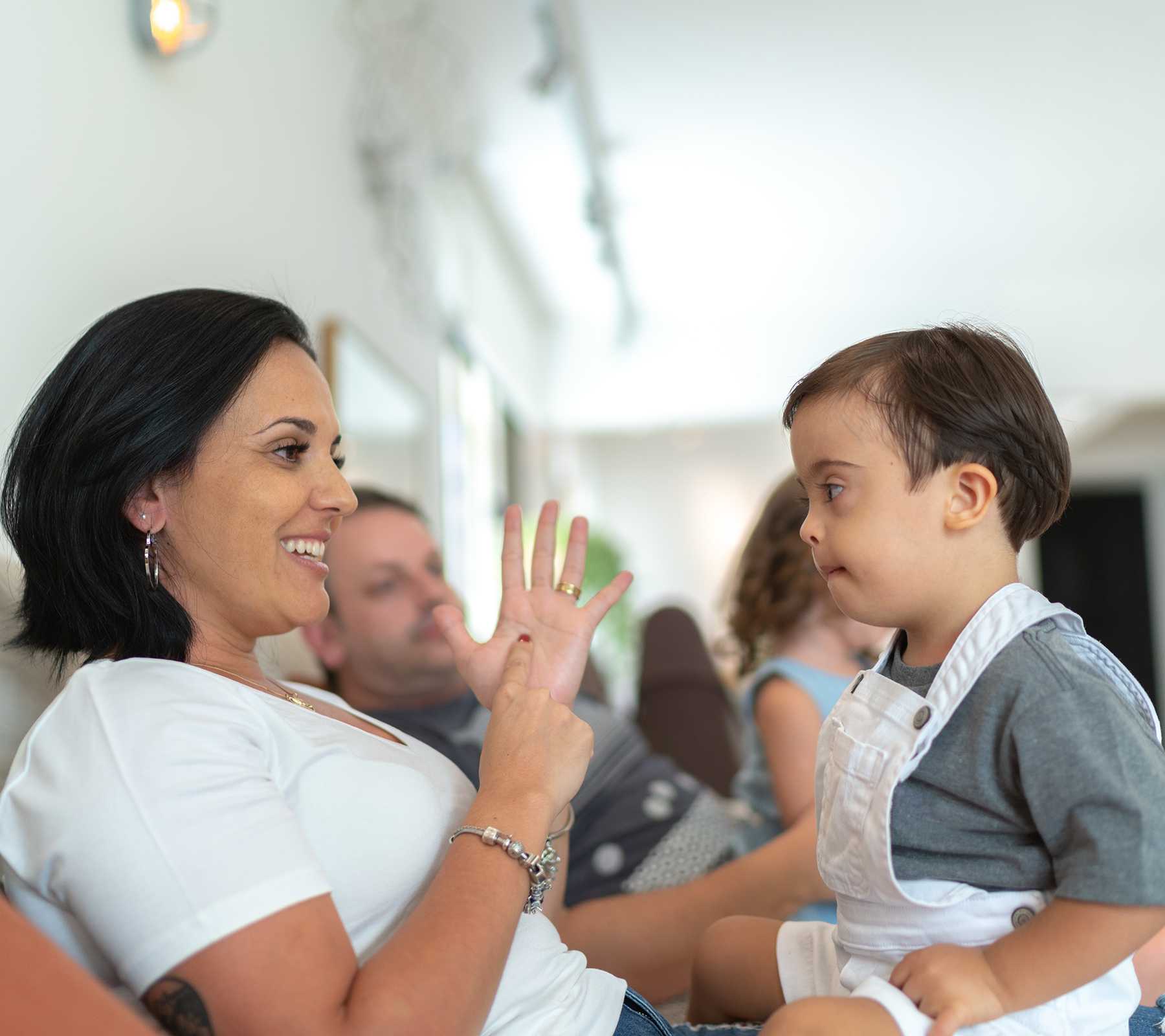 A mother and a son sitting on a couch. The mother signs to the son.