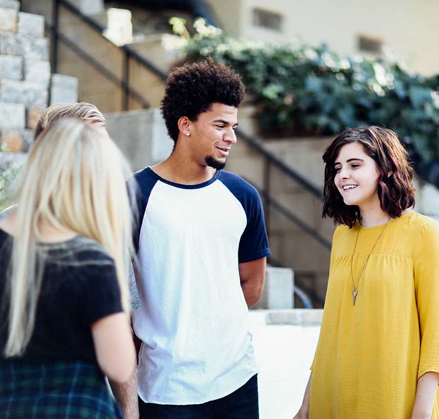 A group of three young friends stand in a circle talking.