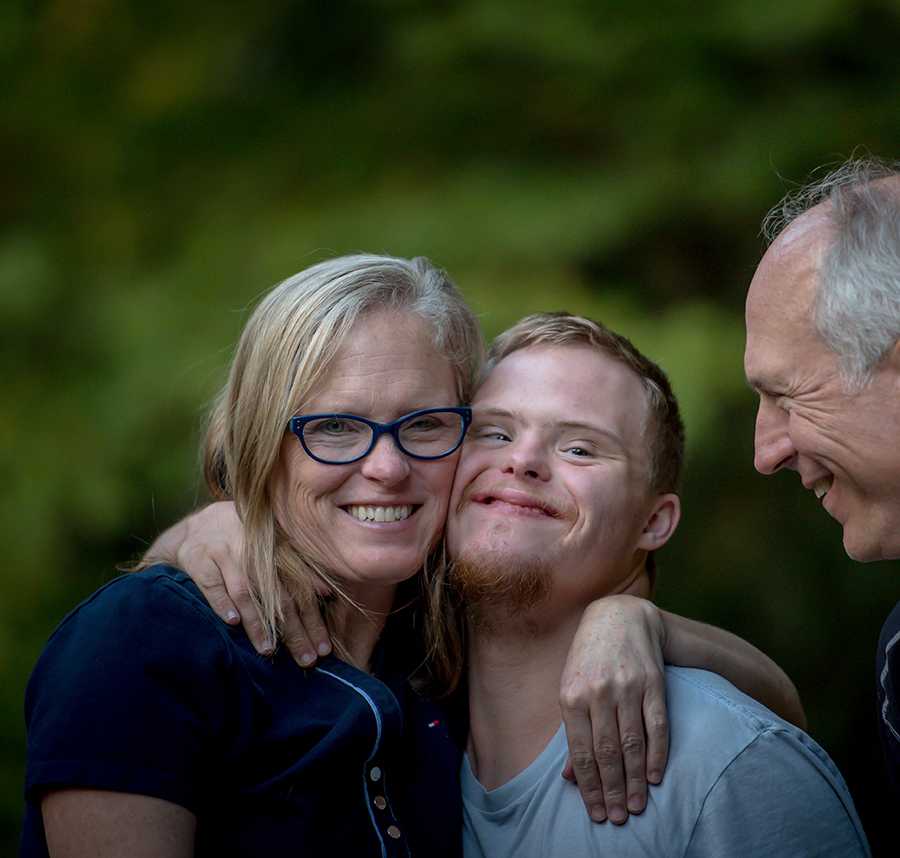 A mother hugs her son with Down syndrome. They are both smiling at the camera.