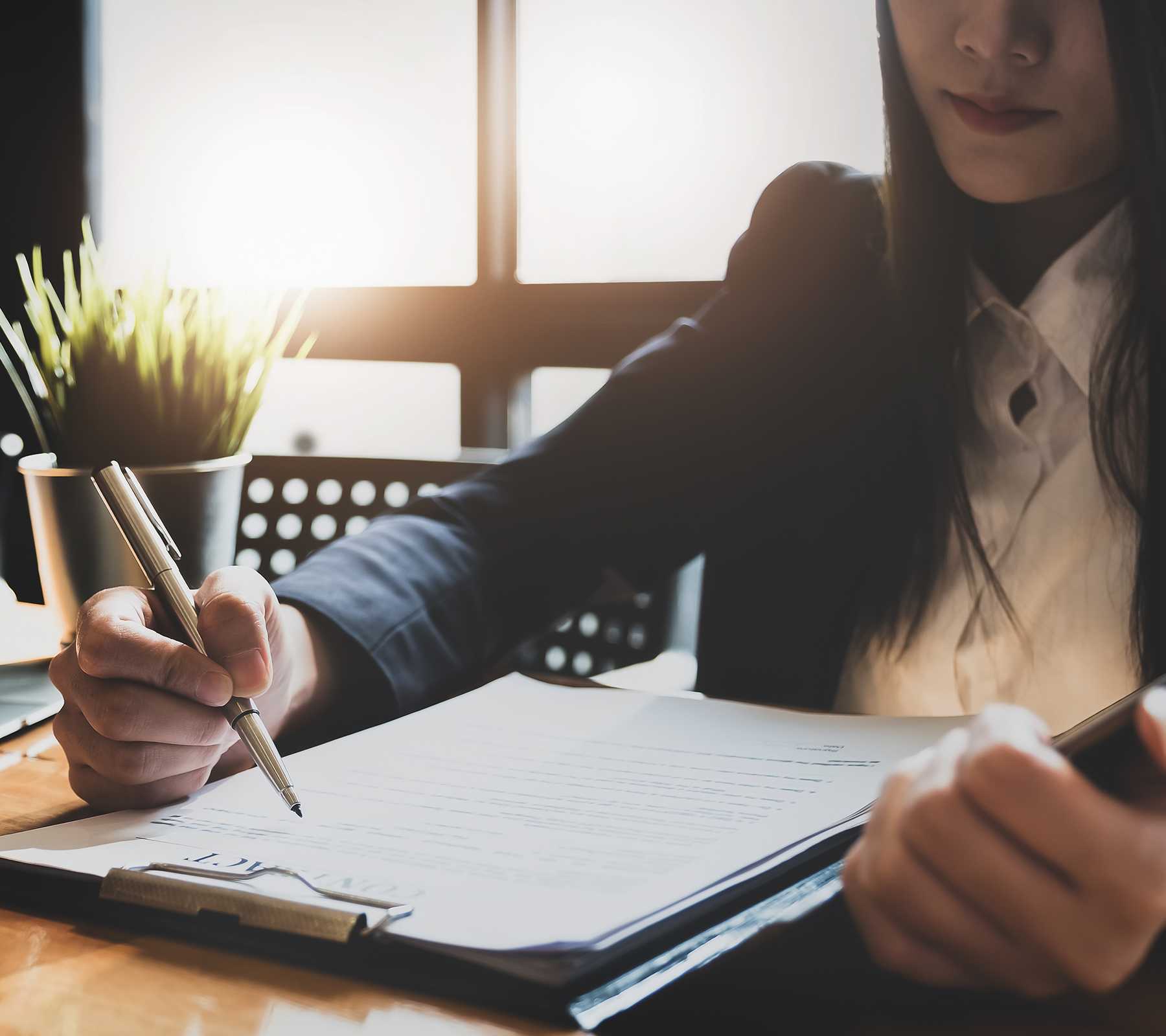 Professional woman in suit, holding pen and reading a contract or agreement.