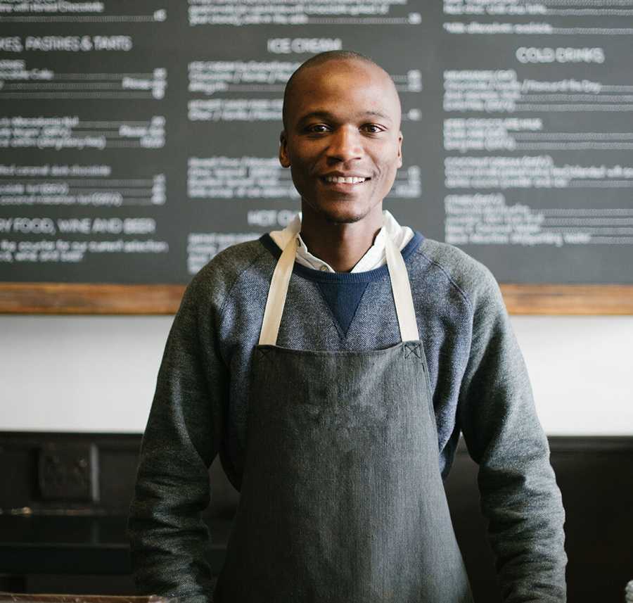 A man with an apron smiles behind the counter of a Cafe.