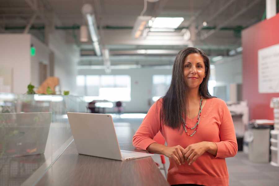 A woman standing at a desk with a laptop in an office environment