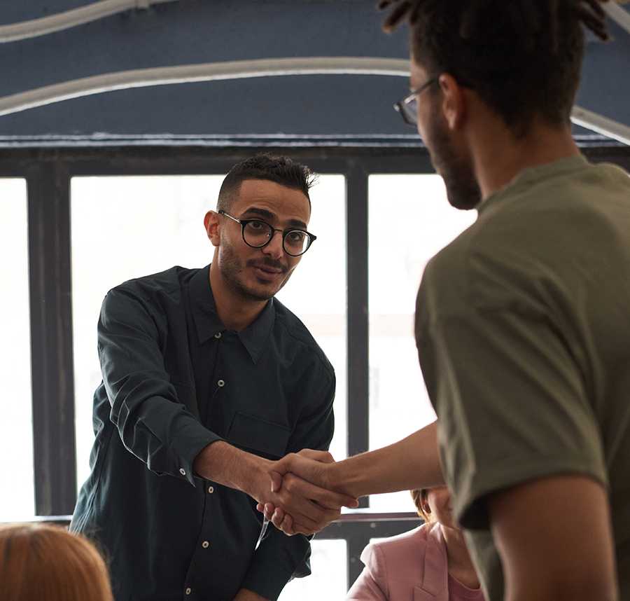 Two men shake hands across a table. They are both dressed in business gear.
