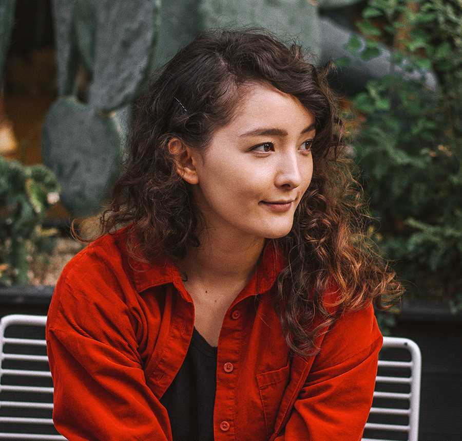 A young woman with curly hair smiles at something in the distance