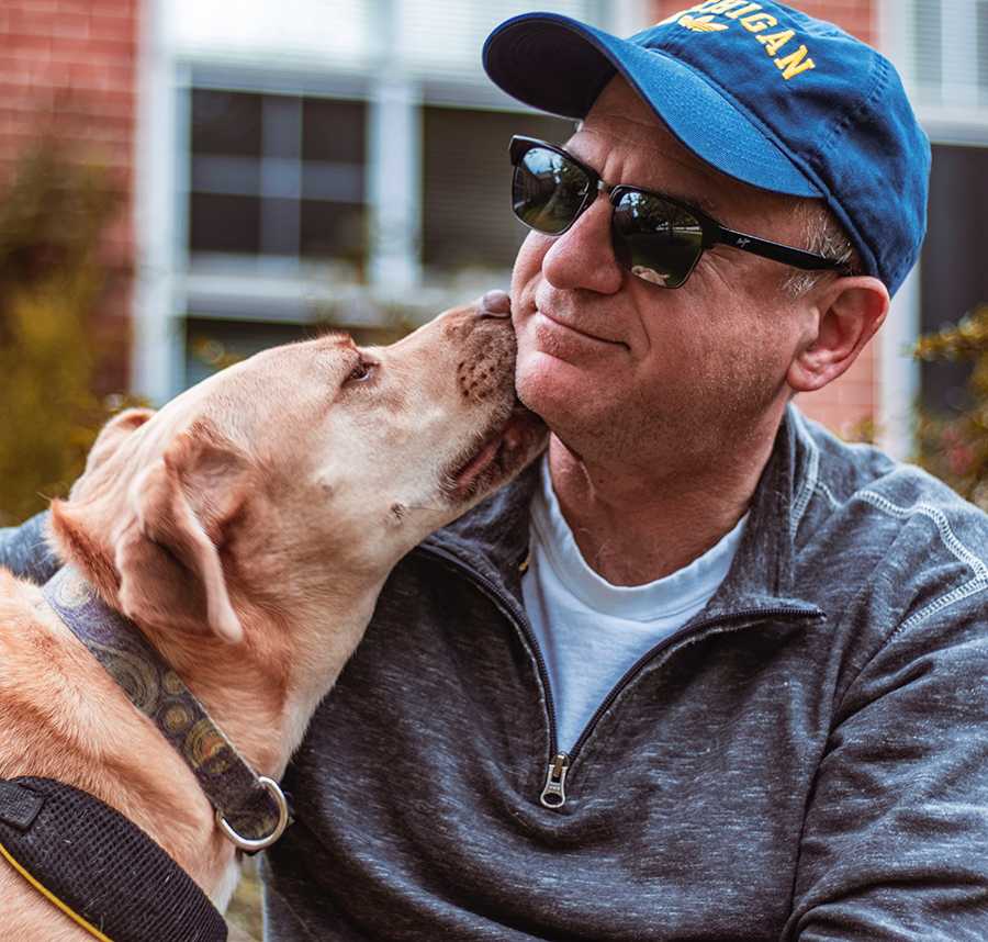A blind man sits whilst his dog licks his face