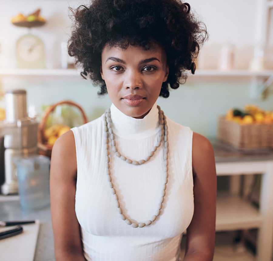 A young black women in a white top looks directly at the camera.