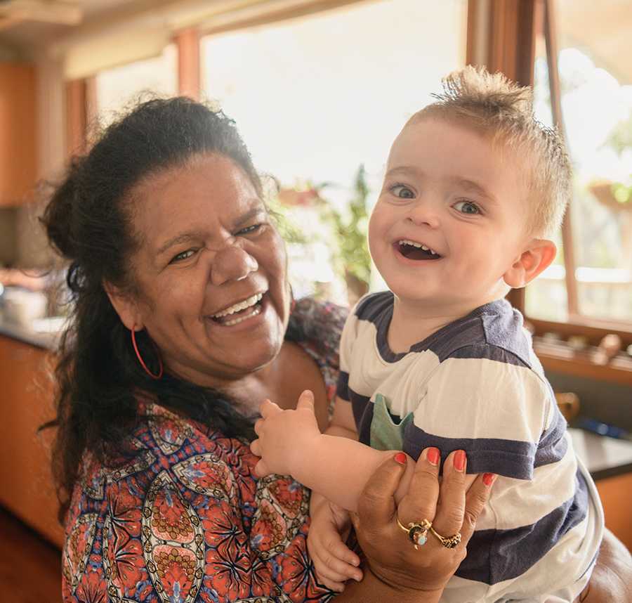 An Aboriginal woman laughs with her grandson in a kitchen.