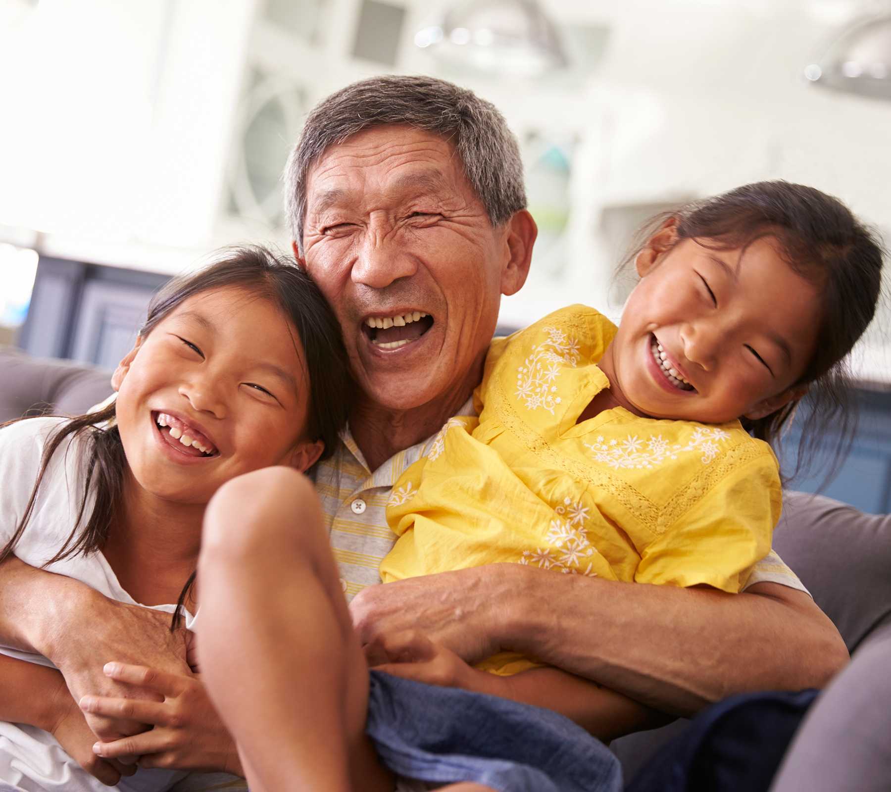 Grandfather and granddaughters relaxing on sofa at home.